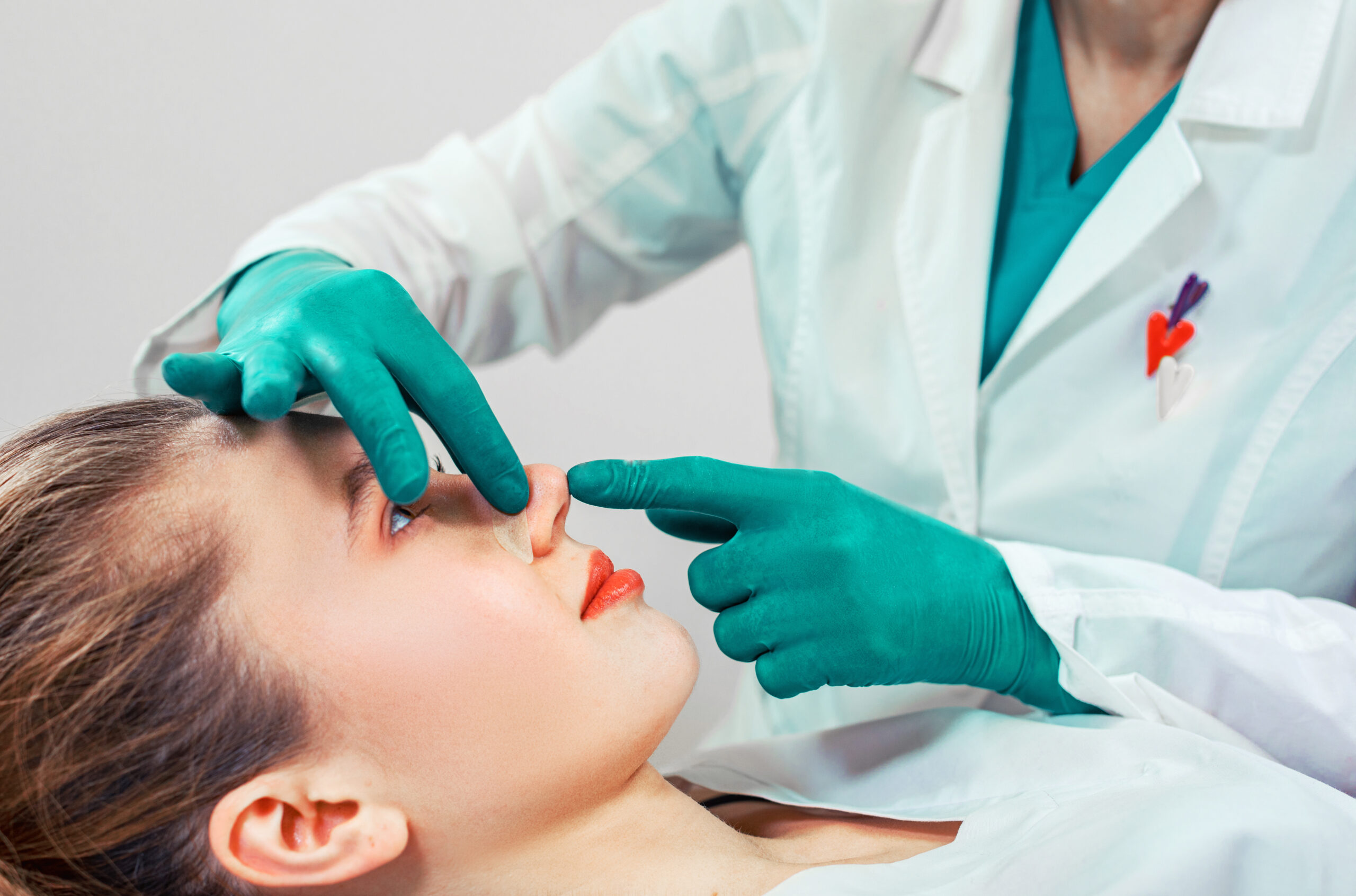 Healthcare professional in teal gloves and a white coat examines the patient's mouth during a dental checkup.