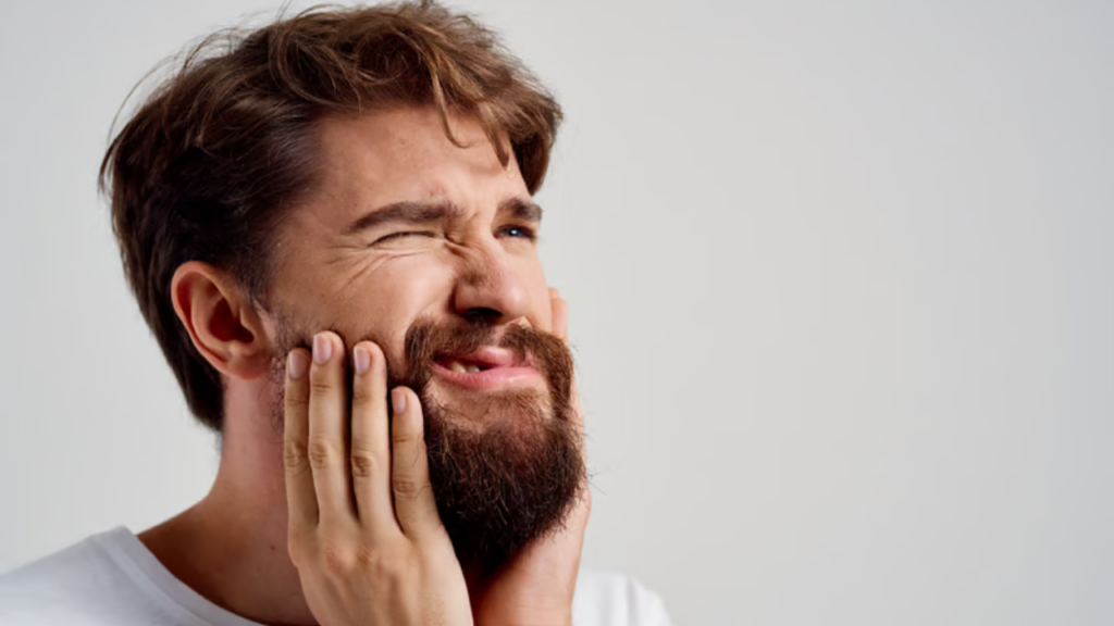 Man with a beard pinching his cheeks with both hands and squinting, making a goofy grimace.